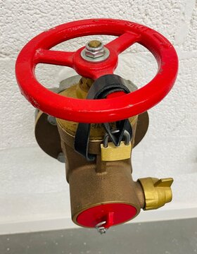 Locked red handwheel valve mounted on a textured wall for building fire safety equipment