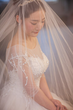  Portrait of elegant Asian bride in lace wedding dress and veil, soft natural window light, bridal morning preparation