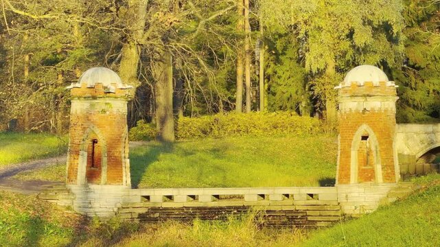 Red brick towers stand beside a stone cascade in Catherine Park, Pushkin, Russia. Golden autumn trees line the lawn, creating a serene, peaceful feeling.