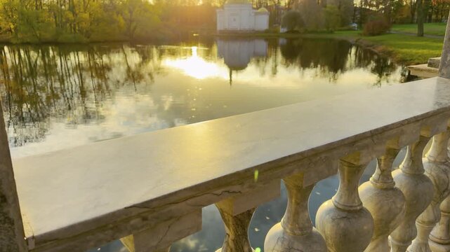 Golden sunlight reflects on the calm lake seen from a marble balustrade. A serene slow motion view in Catherine Park, Pushkin, Russia inspires warm peace and gentle wonder.