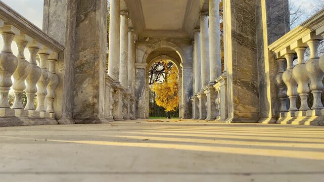 Marble columns cast long shadows along the gallery of the Marble Bridge in Catherine Park, Pushkin, Russia. Golden autumn light fills the space, inspiring peaceful, majestic feelings.