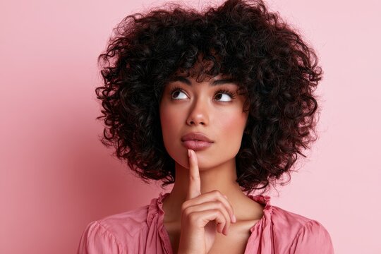 Thoughtful portrait of a woman with natural curls in a pink top, pink backdrop