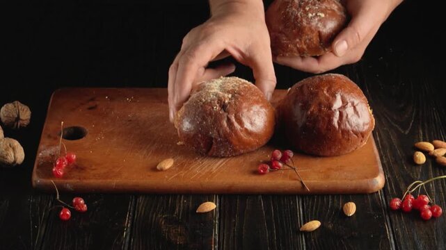 Hands arrange three rustic round loaves on a wooden cutting board with almonds and red berries on a dark tabletop, overhead food styling scene