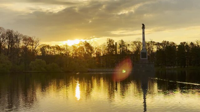Golden sunset light glows over the Chesme Column on the Great Pond in Catherine Park, Pushkin, Russia, in slow motion. The scenic view inspires awe and peaceful joy.