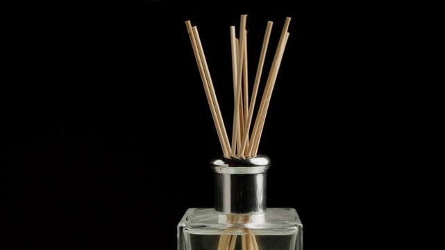 Rotation of a wooden reed sticks in an elegant glass aroma diffuser bottle with a silver cap against a black background