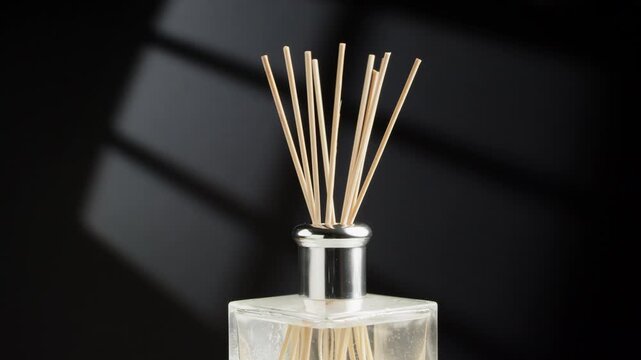 Rotation of a wooden reed sticks in an elegant glass aroma diffuser bottle with a silver cap against a dark background