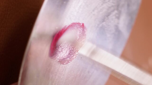 Vertical video. Cosmetic makeup. Artist palette. Unrecognizable female cosmetologist hand mixing pink red cream texture using stainless steel brush.