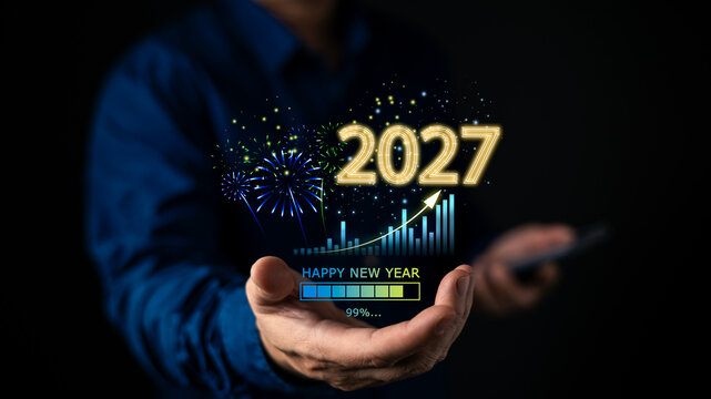 Businessman holding glowing 2027 happy new year hologram with growing graph and 99 percent loading bar. Represents future financial success, business growth, and technology progress.