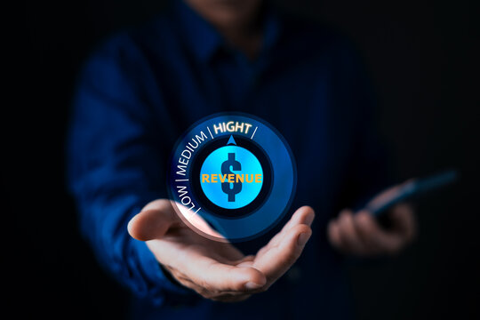 Businessman holding glowing digital hologram showing revenue gauge pointing to high. Concept of financial growth, business success, increasing profit, and wealth management strategy.