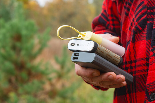 Close up of a person holding multiple portable power banks outdoors. Rechargeable battery packs provide mobile power for smartphones and electronic devices while traveling, camping or hiking.