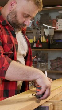 Vertical video. Measuring wood. Joinery workshop. Male carpenter with tape try square marking pencil lumber plank before cutting in industry interior.