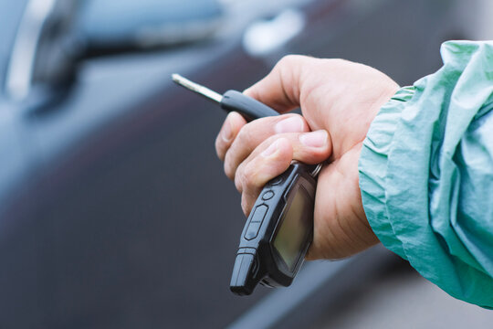 Hand holding car key fob with remote alarm control near vehicle close up. Car security system, remote starter or automotive technology concept.