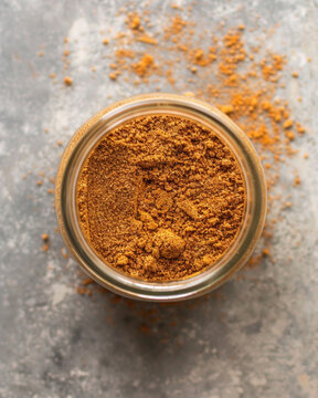 Top view professional cookbook photography of Lebanese seven spice powder (baharat), warm reddish-brown spice powder in a small glass jar, minimal elegant 