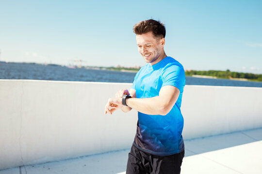 Man checking fitness watch while jogging along a sunny waterfront path