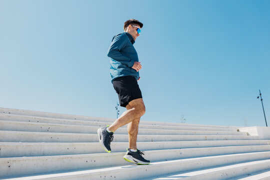 Energetic man jogging down outdoor steps under bright blue sky