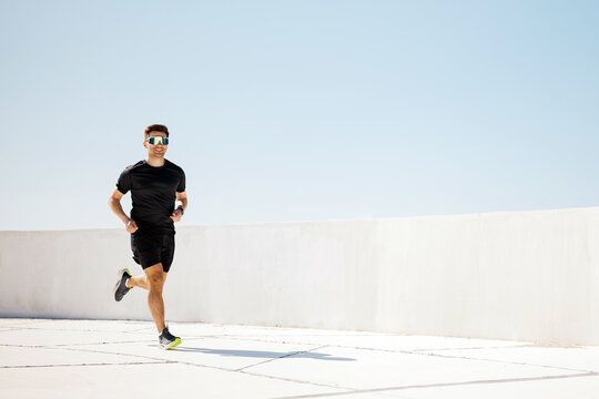 Man running on a sunny day at a modern outdoor track with a clear blue sky