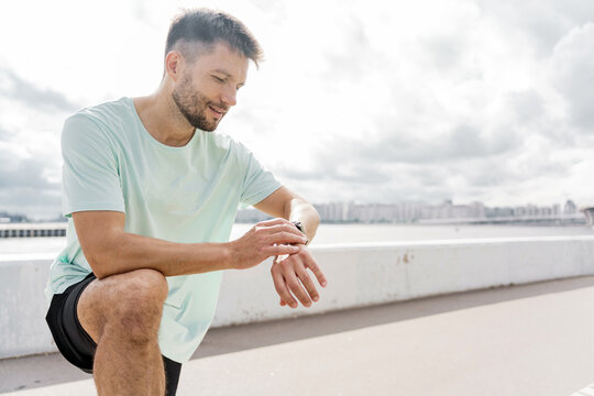 Jogger checking his smartwatch while resting near waterfront in a bright afternoon