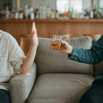 Person refusing a glass of whiskey offered by a friend in a bar setting