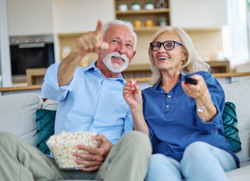Portrait of an elderly senior happy couple watching tv together eating popcorn at home