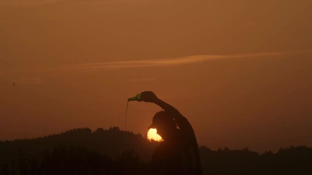 Silhouette of an asturian man pouring traditional cider from above his head at sunset during summer solstice in spain