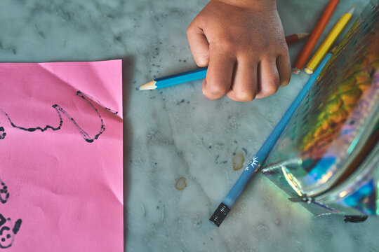 Overhead of a Child's Hand with Colored Pencils and a Drawing on Marble