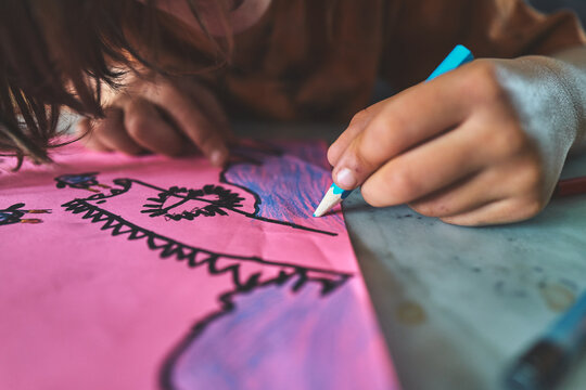 Close-Up of a Child's Hand Coloring with a Blue Pencil on Pink Paper