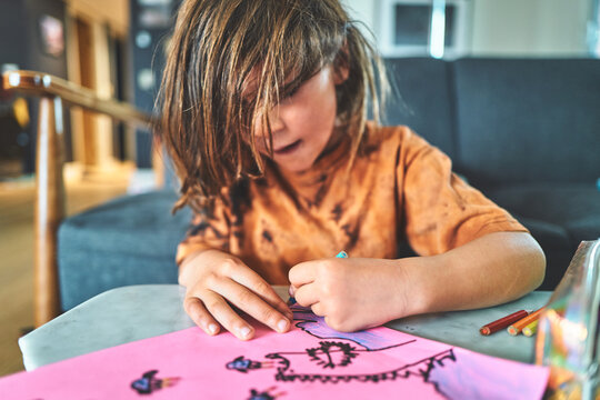 Boy Drawing on Pink Paper with Colored Pencils at a Table
