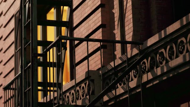Sunlight casts strong shadows on the metal fire escape stairs attached to the brick wall of an old building during the afternoon