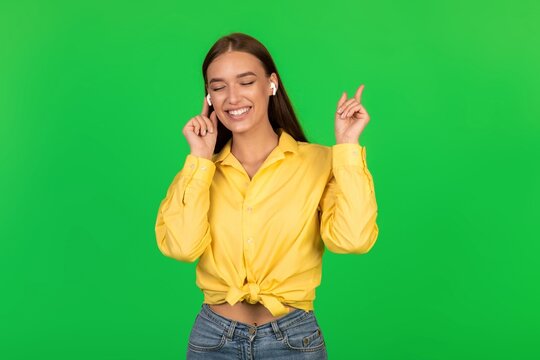 Smiling Young Woman With Caucasian Features Enjoying Music While Listening Through Wireless Earbuds At Home. Joyful Vibe In Modern Living Space, Relaxed And Engaged With Music. Lifestyle Concept.