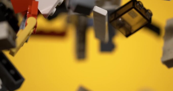 Slow motion Building toy pieces scatter and rotate in midair, isolated on yellow. Colorful plastic bricks, connectors and specialty shapes highlight modular construction and imaginative play.