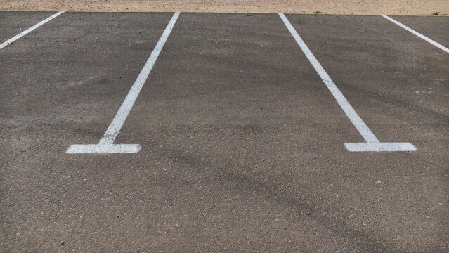 Empty parking space on dark gray asphalt marked with two white painted lines ending in T-shaped bars, vacant parking spot in a car park with visible road markings and no cars in an outdoor parking lot