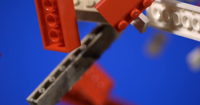 Slow motion Super slow motion Colorful construction toy bricks float and rotate against blue. Loose red, white, gray, and black pieces form lively display of interlocking building components