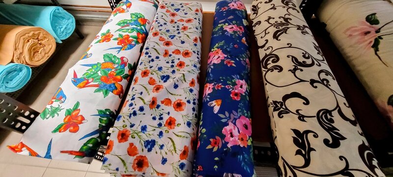 Rolled fabric bolts with colorful printed floral, geometric, and ornamental patterns arranged on wooden tabletop for sewing and upholstery projects with visible textures and details