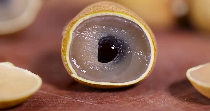 Close-up of juicy white fruit and dark pit of a cut longan, exotic fruit pieces on a rustic table