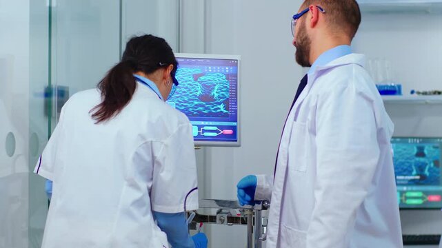 Debate, scientists and computer analysis as two laboratory colleagues discuss molecular data face to face beside a research monitor, for problem solving, critical review and scientific communication.