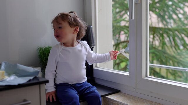 Caucasian mother holds her baby on her lap at the table while supervising her older son doing homework, juggling motherhood and her son's education.