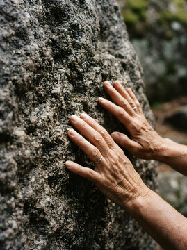 Close-up of hands touching a large textured stone boulder outdoors