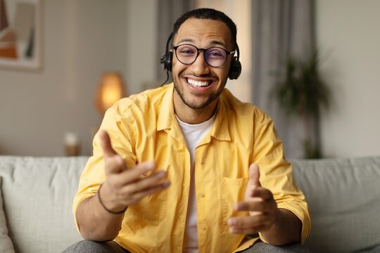 Smiling Black Male Wearing Headset Engaging In Conversation While Sitting On Couch In Home Office Setting, Demonstrating Professionalism And Comfort In Remote Work Environment. Business Concept.