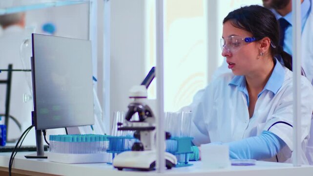 Teamwork, DNA and analysis as two researchers discuss a computer display in a laboratory beside a microscope and test tubes, for biotechnology collaboration, molecular research and scientific review.