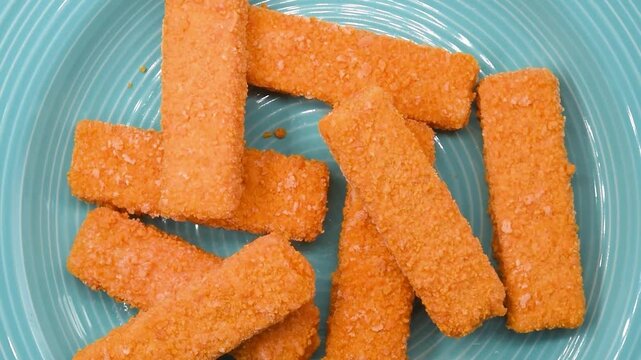 Frozen cod fish fingers rotating on a blue plate. Breaded seafood sticks ready for frying or baking, ideal for fast meals, food ads, or cooking videos