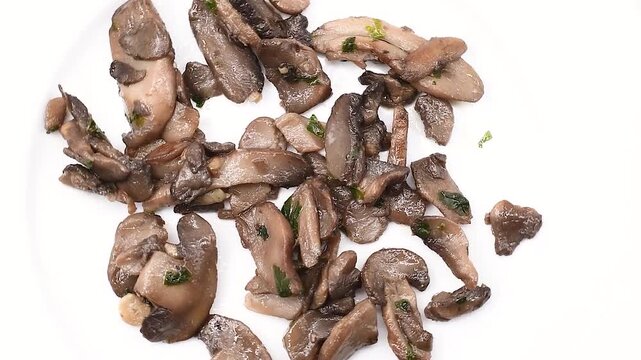 Rustic Button mushrooms Agaricus Bisporus, cooked in a pan with olive oil, garlic and parsley, on a white plate, extreme close-up, rotating video