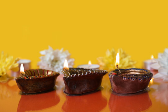 Diya lamps with beautiful flowers and burning candles on color background. Divaly celebration