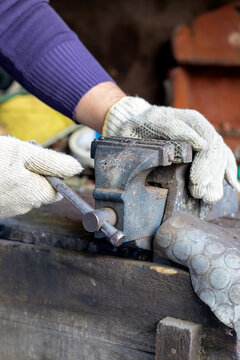 Vertical stock photo of gloved hands tightening a heavy-duty bench vise in a workshop