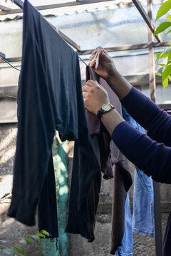 Vertical stock photo of hands hanging wet laundry with clothespin on outdoor clothesline