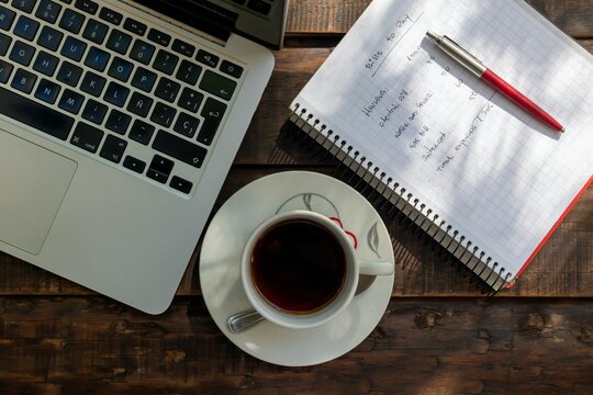 Top view of laptop, coffee cup, and personal finance notebook on wooden desk