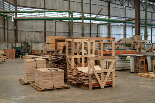 Occupying the factory interior, a woodworking machine stands near neatly stacked wooden pallets and piles of plywood sheets.