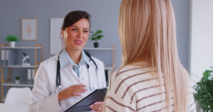 Female doctor support young patient putting hand on her shoulder. Physician sitting in medical clinic giving consultation woman during medical examination in office. 4k video. Slow motion video.