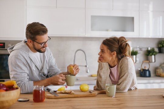Man squeezes lemon into tea while woman with a cold watches at kitchen island.
