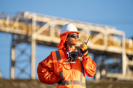 Industrial worker in safety gear communicating by radio beside elevated steel structures