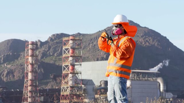 Industrial worker wearing safety equipment speaking on a walkie talkie at open pit mine plant